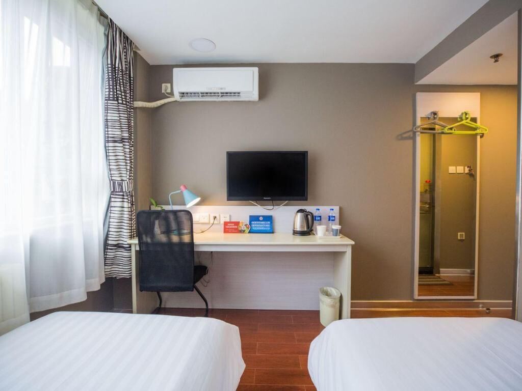 Habitación de hotel con dos camas, un escritorio, televisor de pantalla plana, aire acondicionado y zona de ducha con barra para toallas.