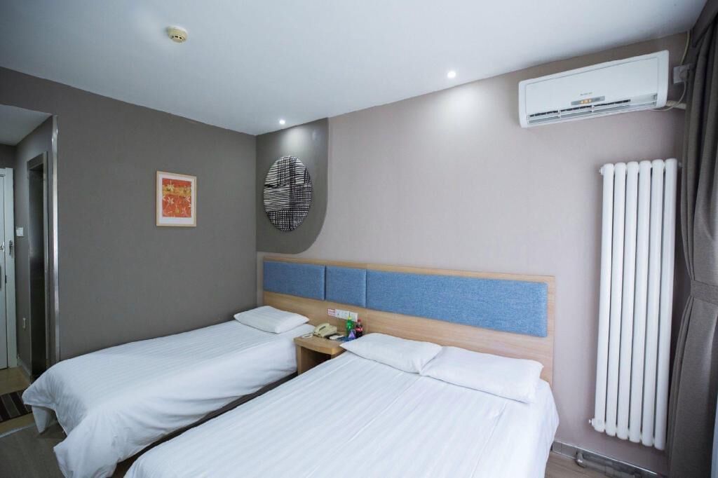 Ein Hotelzimmer mit zwei Einzelbetten, einem Nachttisch mit Telefon und Flasche, einer Wand-Klimaanlage und einem Heizkörper.