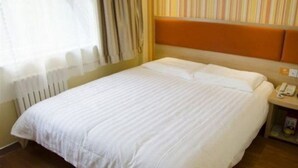 A hotel room with a bed, a nightstand with a phone, and a window with curtains.