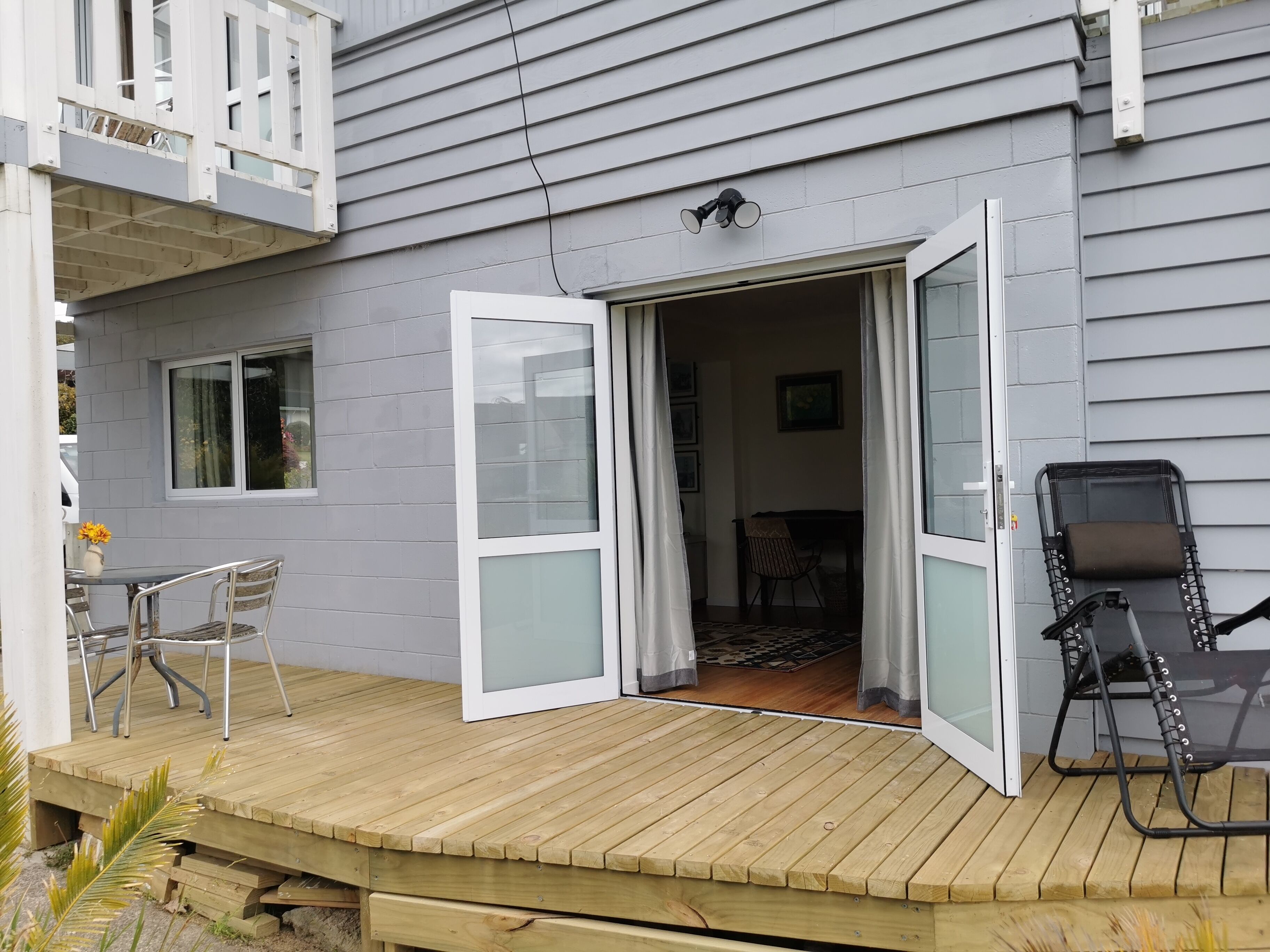 A wooden deck with a glass door leading to an interior space, a chair, and a table.