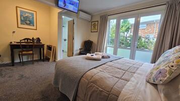 Quarto de hotel com cama, escrivaninha com cadeira, televisão na parede e janela com cortinas.