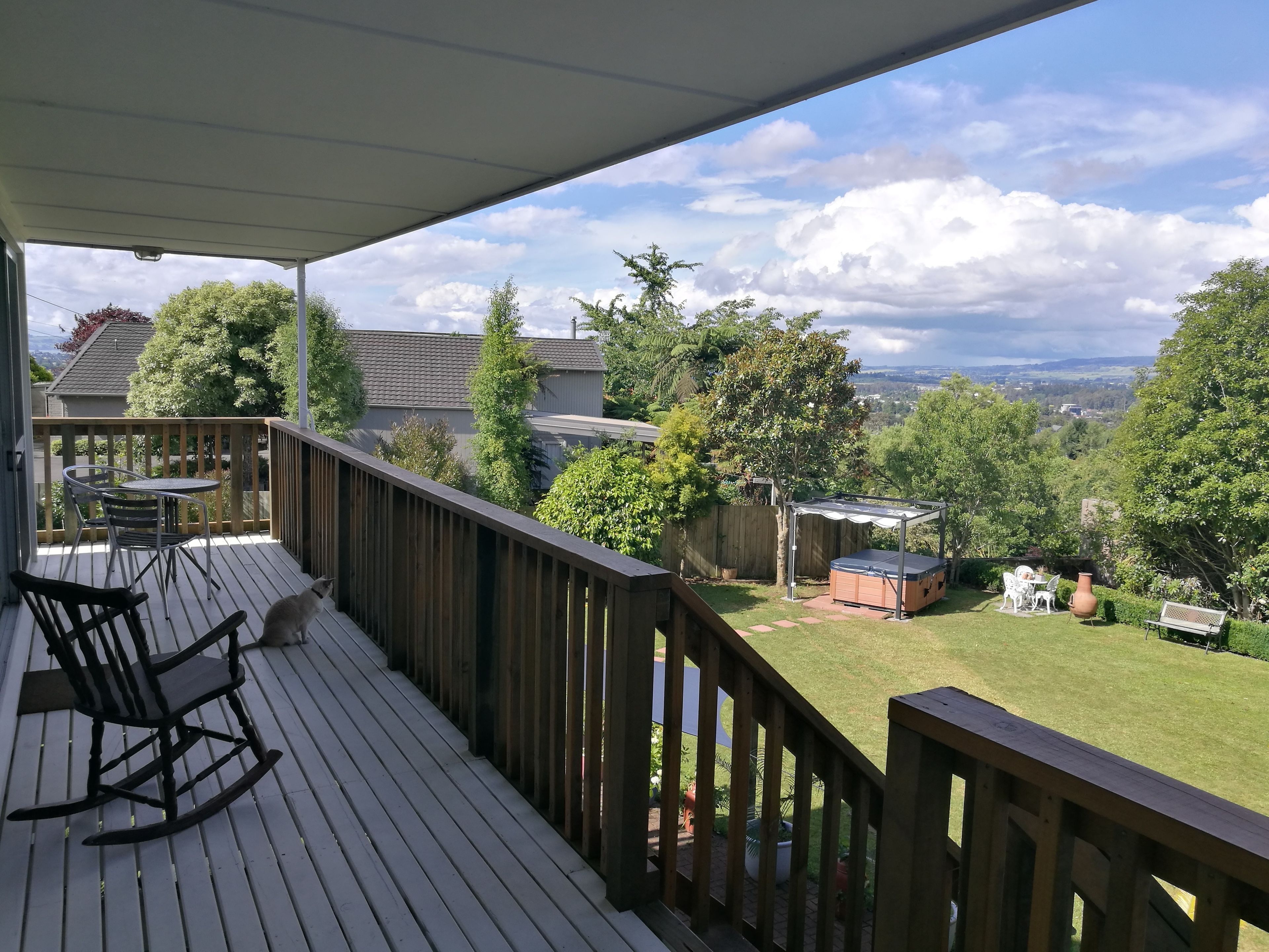 A wooden deck with a table and chairs, a rocking chair, and a hot tub in the background.