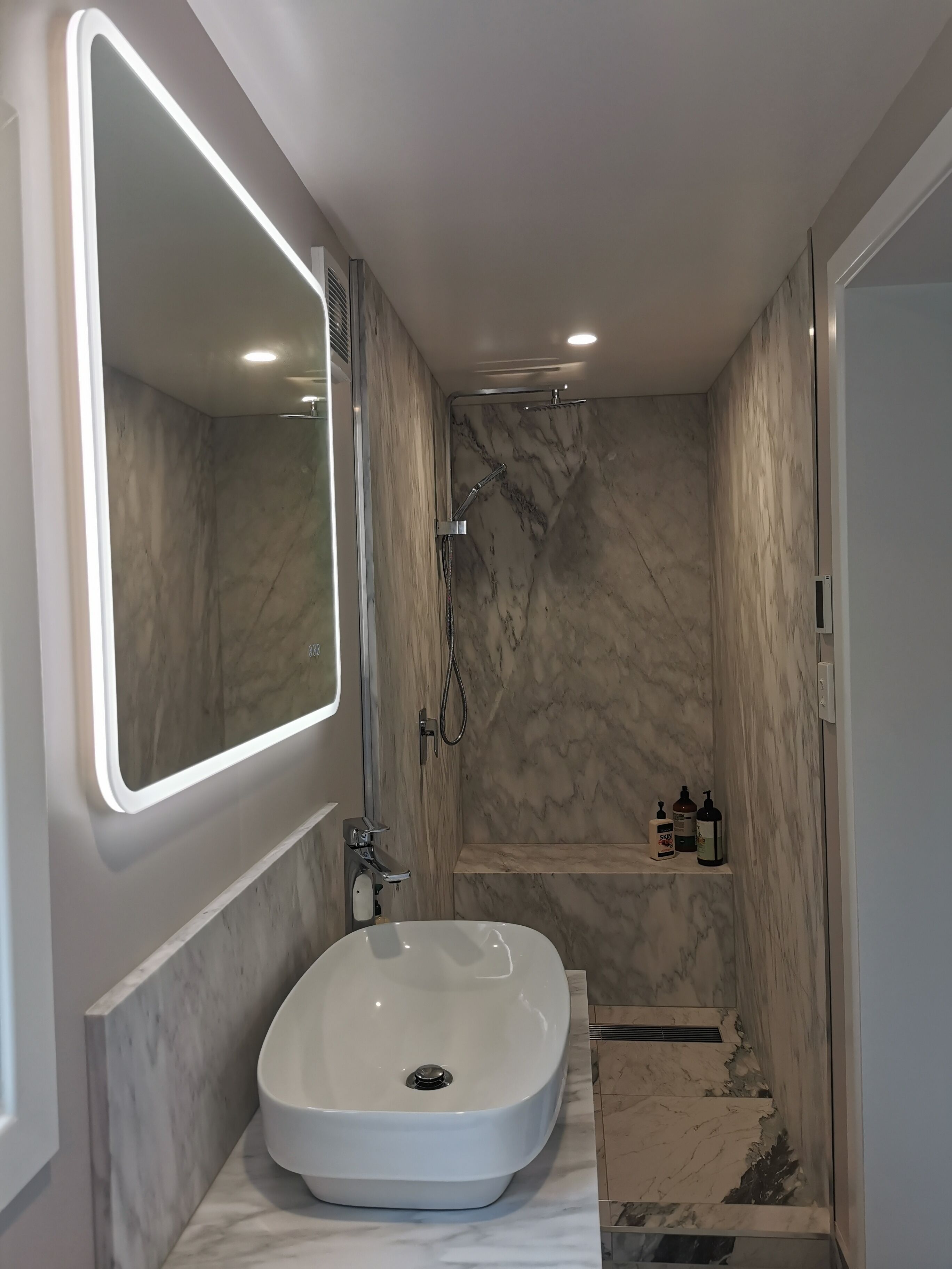 A modern bathroom with a white sink, a large mirror, and a shower area.