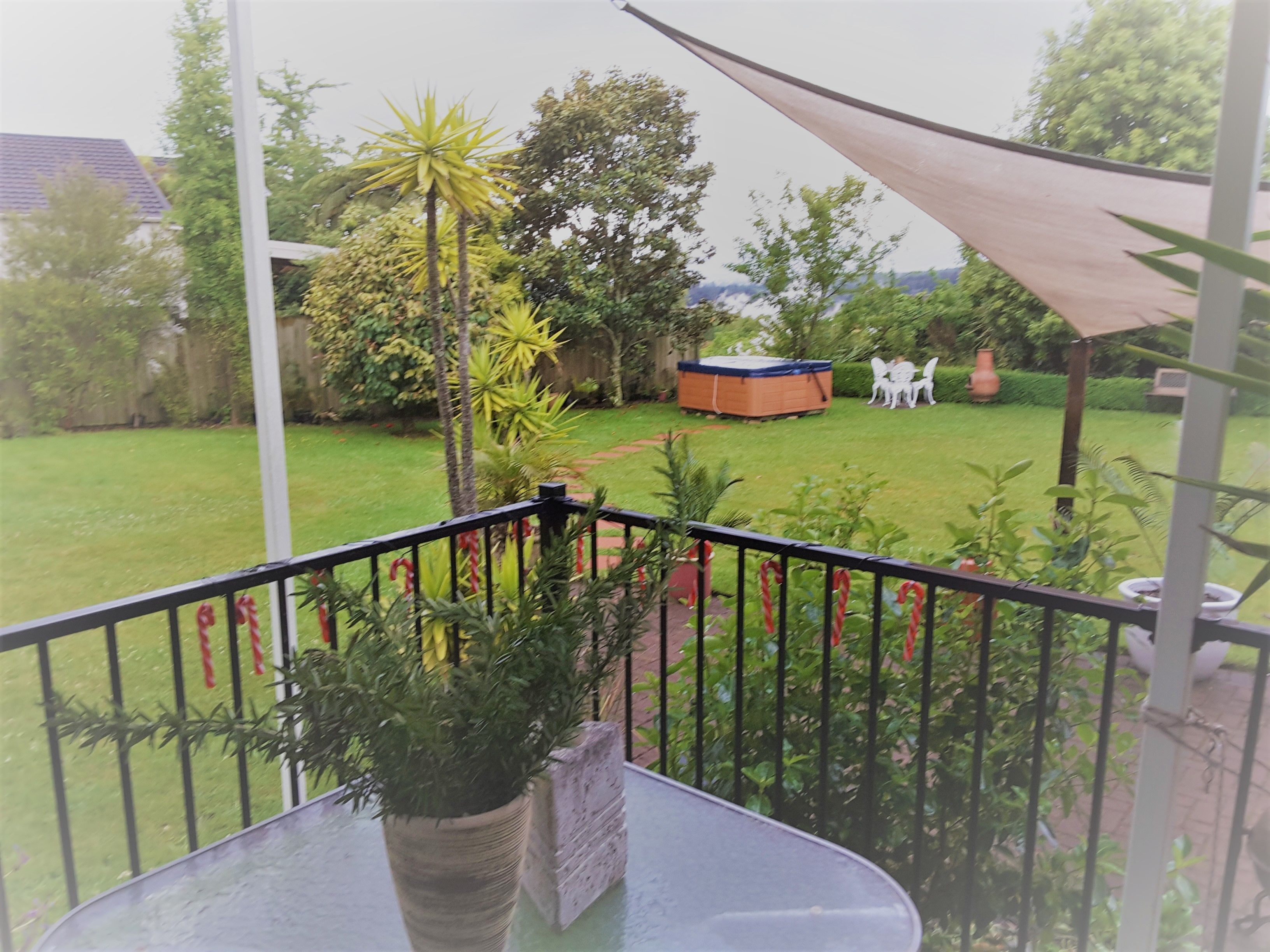 A balcony with a view of a garden, a hot tub, and a patio area with chairs.