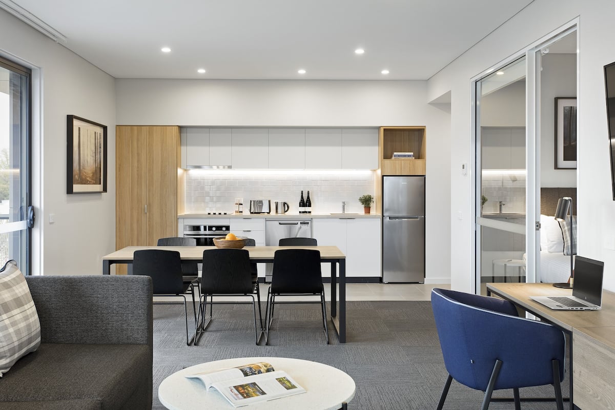 A modern kitchen with white cabinets, a stainless steel refrigerator, and a dining area with a table and chairs.