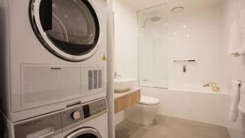 A laundry area with a front-loading washer and dryer, a glass shower enclosure, a toilet, and a bathtub.