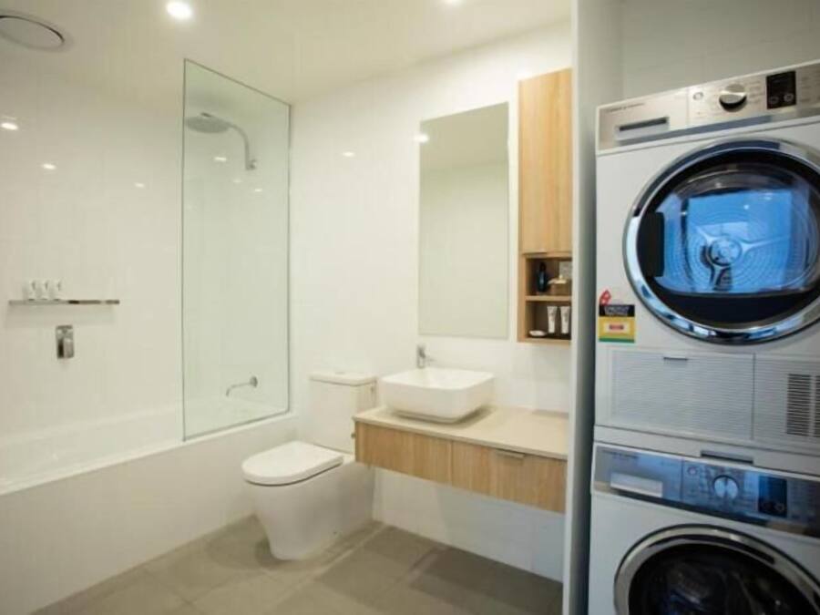 A modern bathroom with a glass shower enclosure, a toilet, a sink, and a stacked washer and dryer unit.