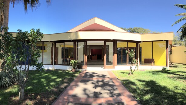 A modern house with a curved roof, large glass doors, and a well-maintained lawn. - La Casa de Cariari Al Golf (La Asunción)
