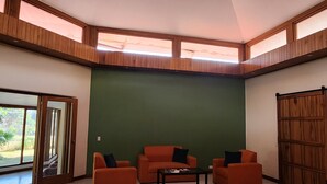 A spacious room with a high ceiling, large windows, and a skylight. There are three orange sofas and a small table. - La Casa de Cariari Al Golf (La Asunción)
