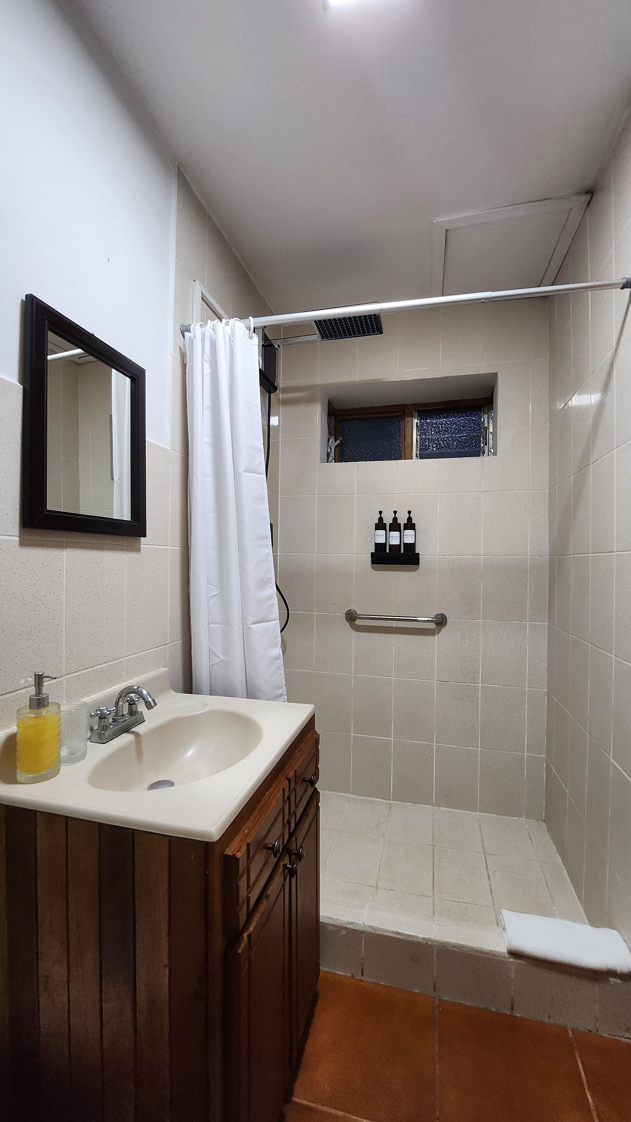 A bathroom with a sink, mirror, shower, and toiletries.
