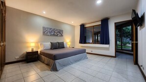 A bedroom with a bed, nightstands, a window with curtains, a painting on the wall, and a door leading outside. - La Casa de Cariari Al Golf (La Asunción)