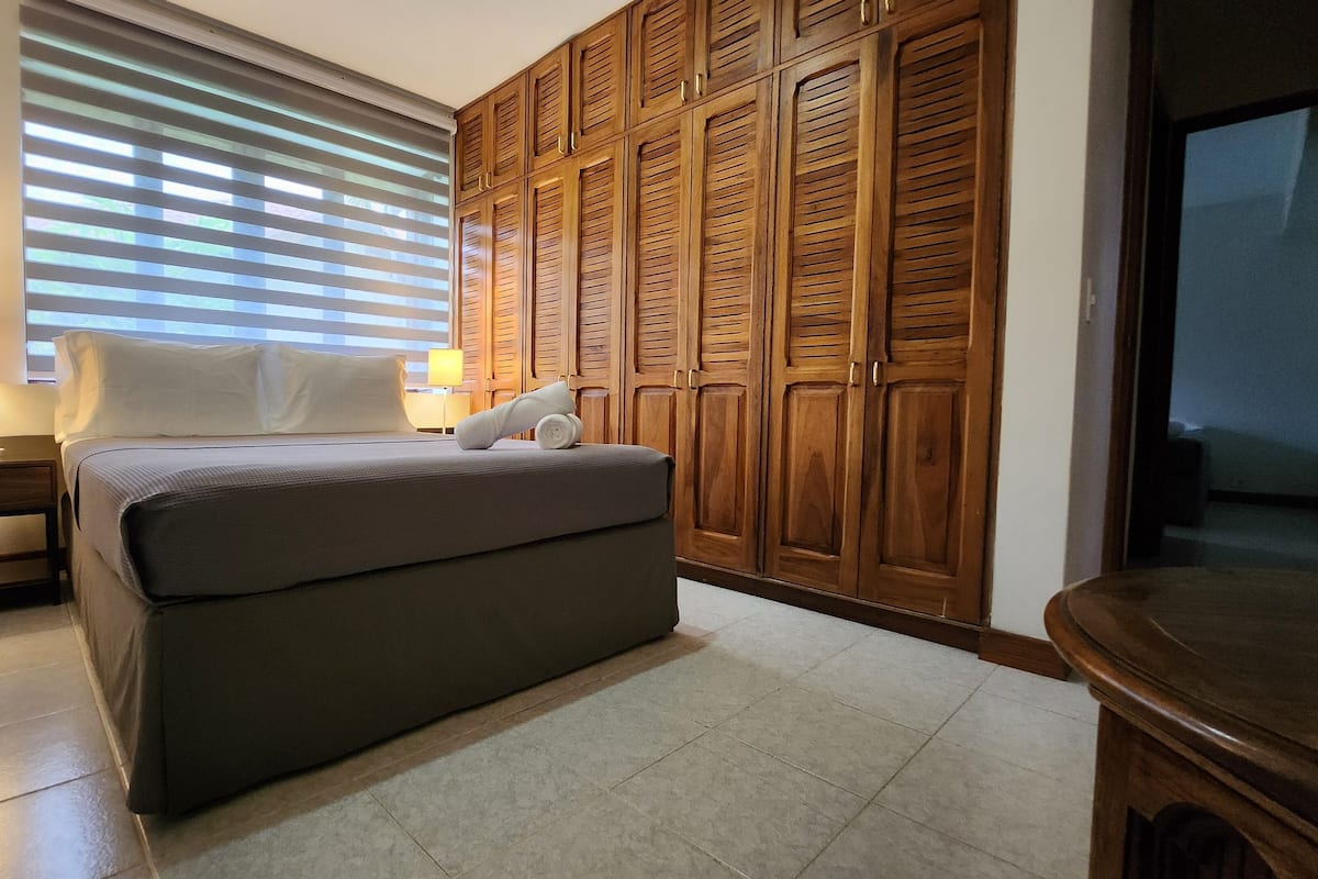 A bedroom with a bed, a nightstand, a lamp, a wardrobe, and a television.