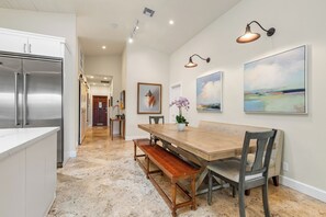 Une cuisine spacieuse dotée d’un grand îlot central, d’appareils électroménagers en acier inoxydable et d’un coin repas avec une table et des bancs en bois.
