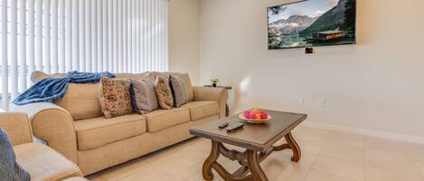 A living room with a beige sofa, a wooden coffee table, and a painting of a mountain landscape on the wall.