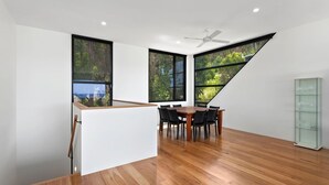 Een moderne eethoek met een houten tafel en stoelen, grote ramen met uitzicht op groen, en een witte roomdivider.