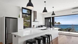 Een moderne keuken met een groot eiland, zwarte barkrukken en uitzicht op zee.
