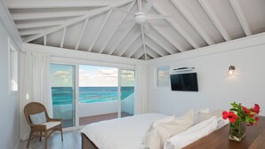 Un dormitorio con una cama grande, una silla de mimbre, una mesa de madera y vistas al océano.