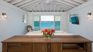Un dormitorio con cama de madera, vista al océano, ventilador de techo y televisor montado en la pared.