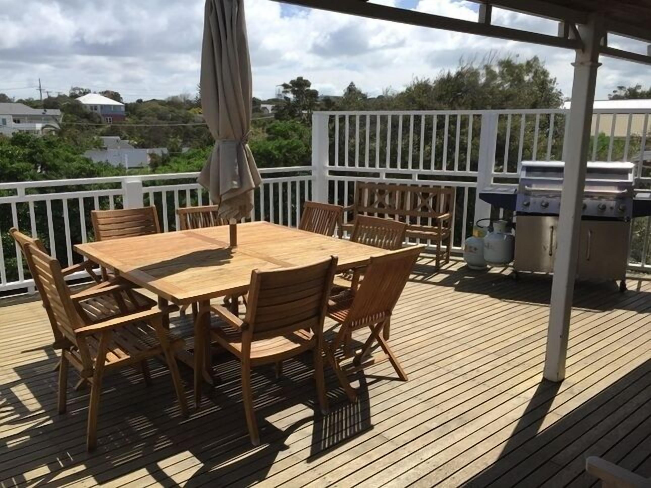 A wooden deck with a table and chairs, a grill, and a white railing.