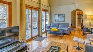 A spacious living room with a grey sofa, a coffee table, a TV, and a dining area with a table and chairs. - Secluded, Fenced Cottage, Hot Tub, Fire Pit, Dog Friendly, Nat’l Park (Miller Beach)