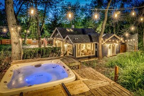 Un espace extérieur accueillant avec un jacuzzi, doté d’une terrasse en bois et entouré d’une clôture en bois et d’arbres.