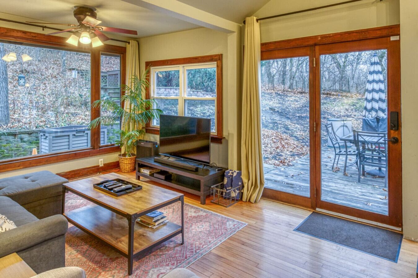 A living room with a TV, sofa, coffee table, and a large window overlooking a deck.