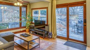 A living room with a TV, sofa, coffee table, and a large window overlooking a deck.
