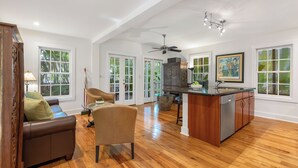 A spacious living area with a wooden floor, a sofa, a chair, a kitchen island with a sink, and a ceiling fan.