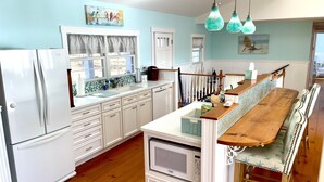 A kitchen with white cabinets, a wooden dining table, and hanging teal light fixtures. - Maine Waterfront Cottage: Nestled on an acre of land, with 500ft of shore front (Newcastle)