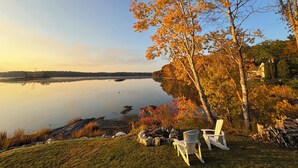 A lakeside view with chairs and a fire pit, surrounded by autumn foliage. - Maine Waterfront Cottage: Nestled on an acre of land, with 500ft of shore front (Newcastle)