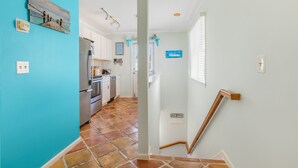 A kitchen with a refrigerator, oven, and sink, a staircase with a wooden handrail, and a blue wall with a decorative piece. - THE QUARTERDECK ~ Colorful & Comfy 2nd Floor 2Ba/ 1Ba Shipyard Unit! (Key West)
