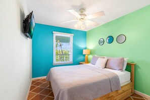 A bedroom with a bed, a ceiling fan, a window with blinds, a lamp, and wall decorations.