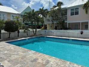 A swimming pool with a white fence, surrounded by buildings with balconies and palm trees.