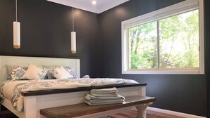 A bedroom with a bed, bedside table, and a window with a view of greenery. - Mt Solitary House – Elite Views | Incredible Comfort (Katoomba)