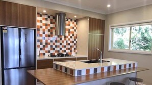 A modern kitchen with a central island, stainless steel appliances, and a checkered backsplash. - Mt Solitary House – Elite Views | Incredible Comfort (Katoomba)