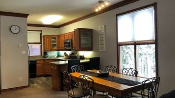 A kitchen with wooden cabinets, a dining table with chairs, a clock, and a motivational poster.