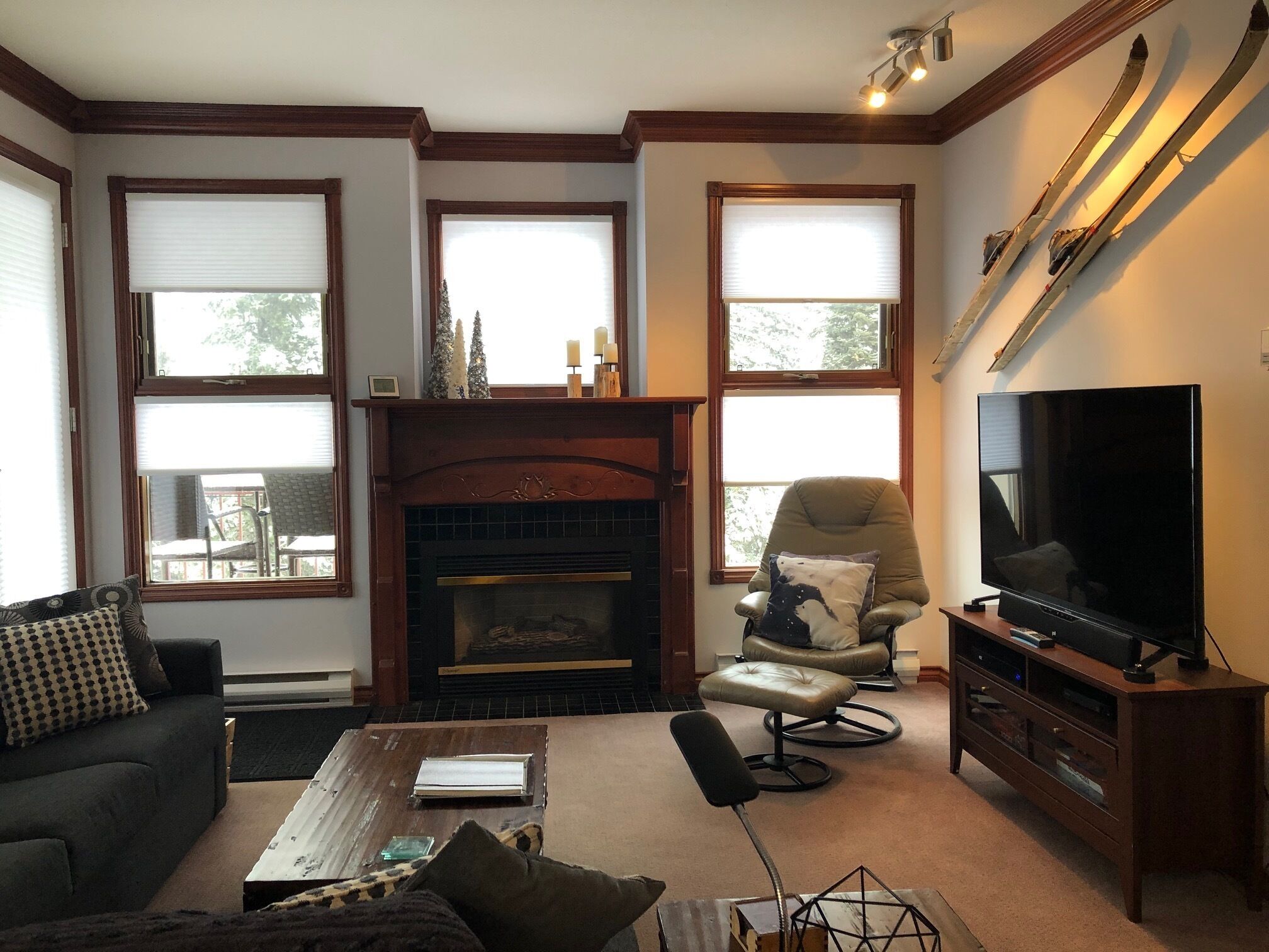 A cozy living room with a fireplace, a comfortable sofa, a television, and large windows.