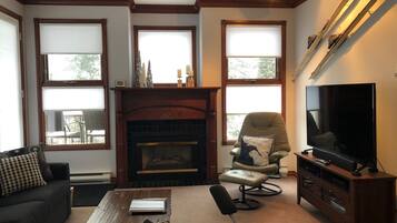 A cozy living room with a fireplace, a comfortable sofa, a television, and large windows.