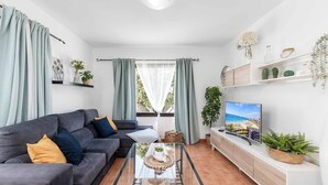 A modern living room with a grey sofa, a glass coffee table, and a TV on a white console.