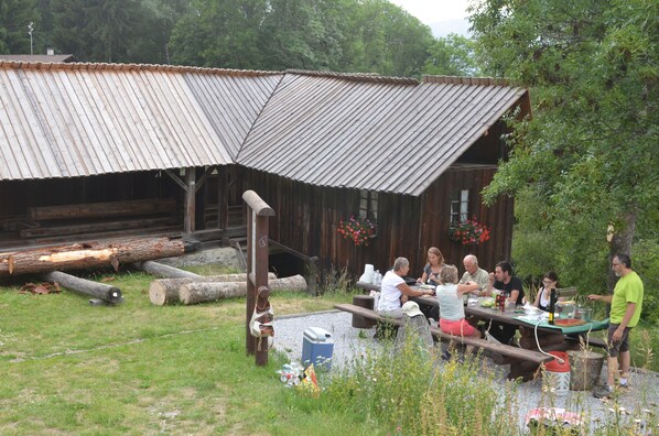 Een rustieke houten blokhut met een golfplaten dak, een picknicktafel en een groep mensen die buiten eten.