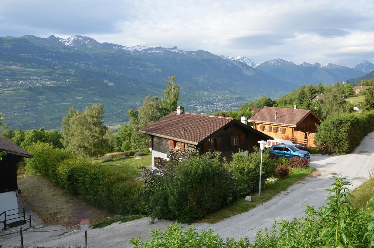 Ein Anwesen an einem Hang mit zwei Holzhäusern, einem Auto und Blick auf die Berge.