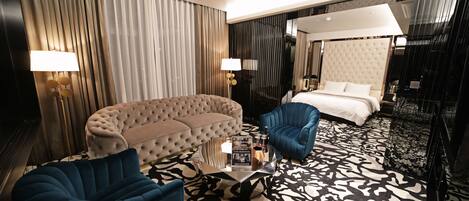 Ein modernes Hotelzimmer mit einer gesteppten Couch, einem blauen Sessel, einem Glastisch und einem gemusterten Teppich.
