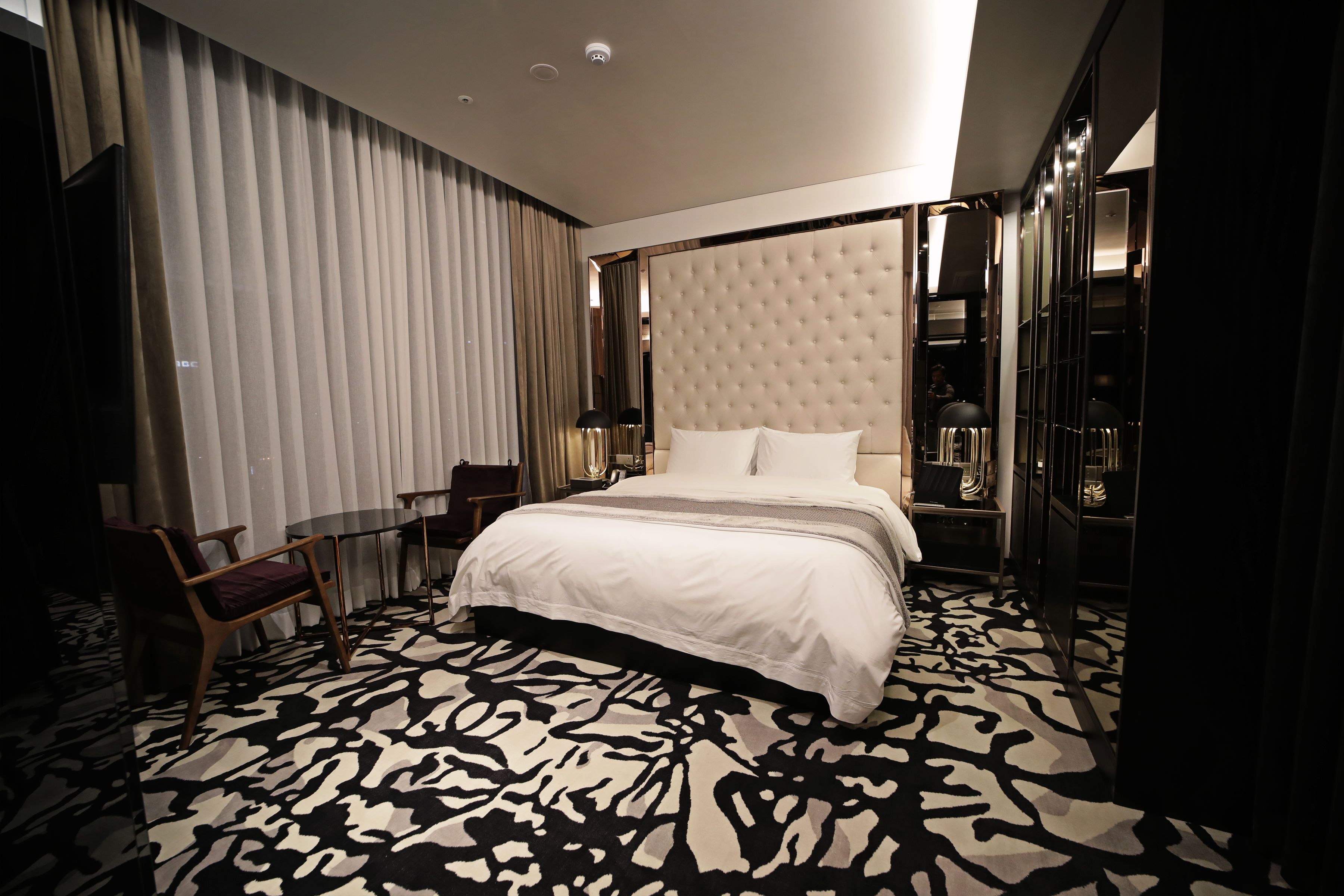 Hotelkamer met een groot bed, een zithoek met een stoel, een tafel en een kamerbreed tapijt met een patroon.