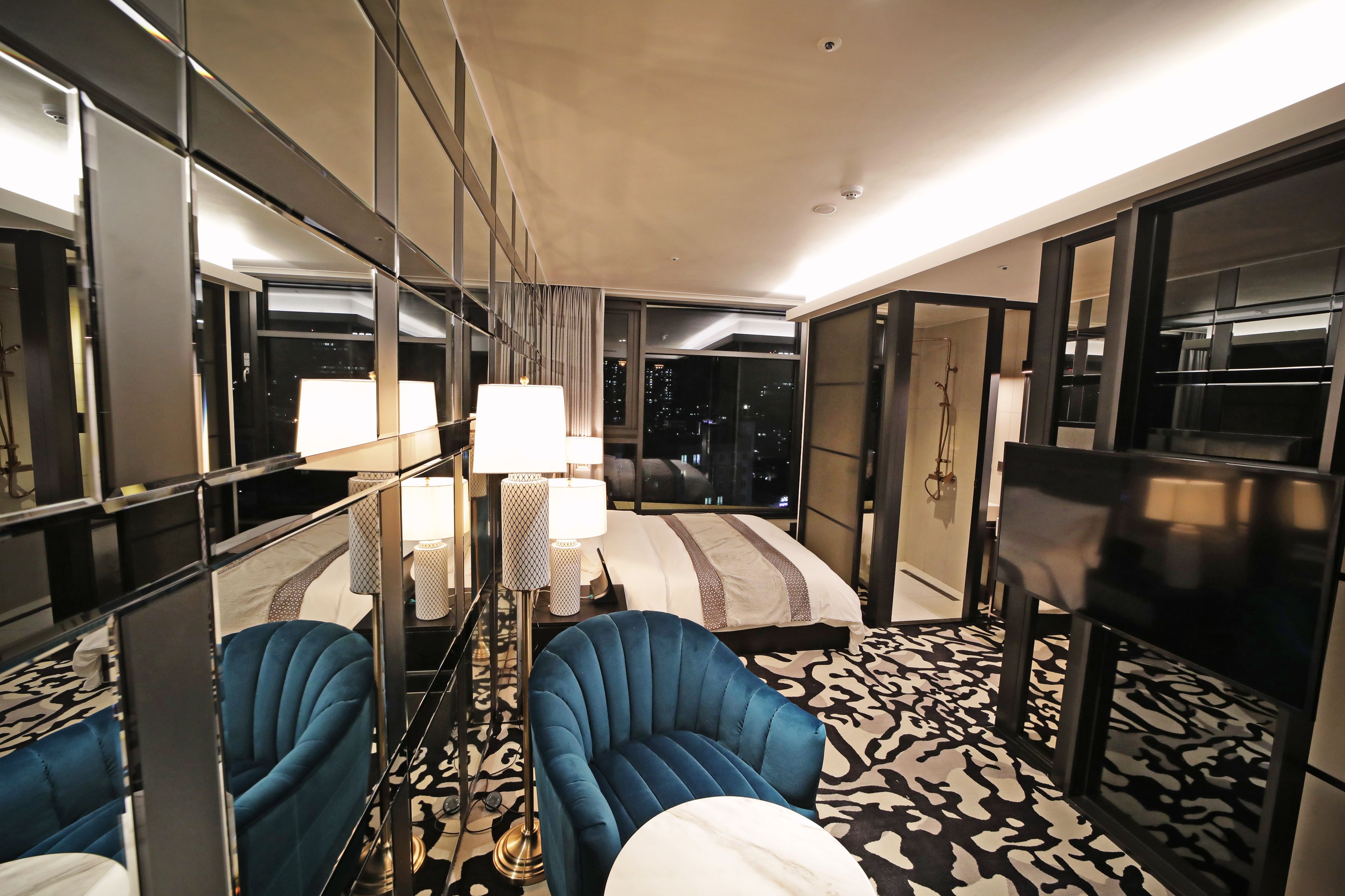Een hotelkamer met een bed, twee fauteuils, een televisie en een groot raam met uitzicht over de stad.