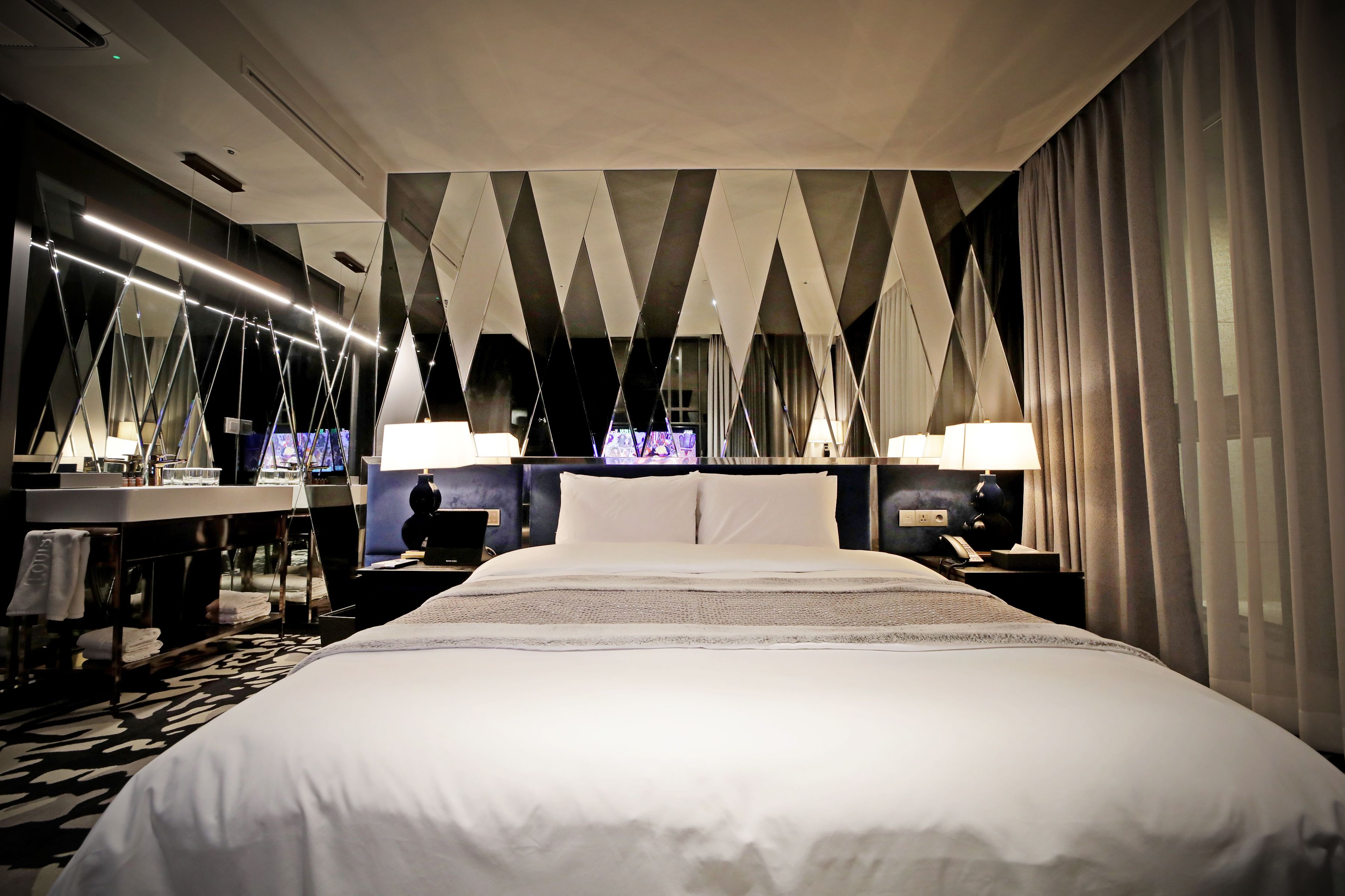 Quarto de hotel com uma cama grande, uma escrivaninha com cadeira, um espelho e uma televisão.