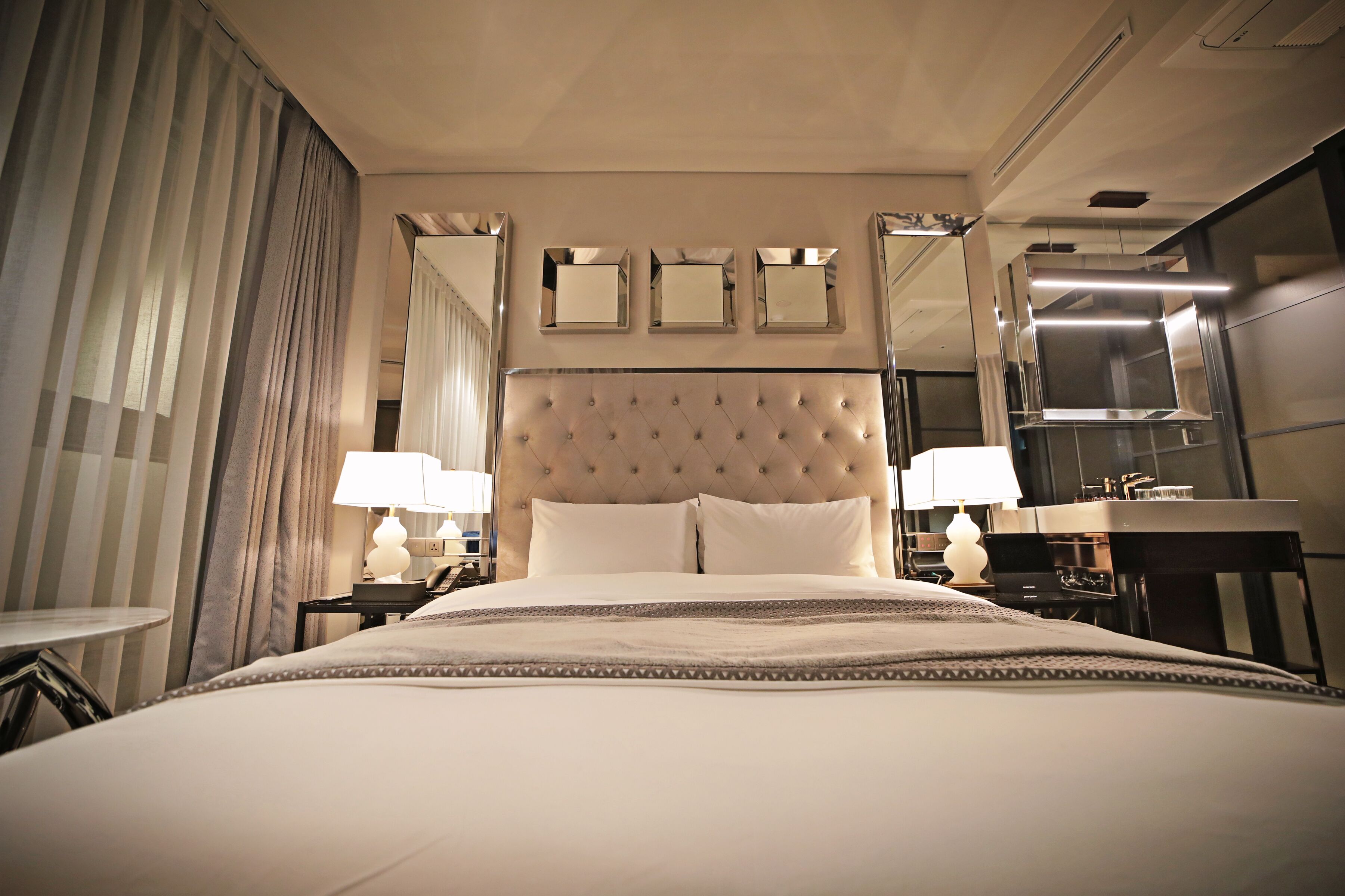 Une chambre d’hôtel avec un grand lit, deux tables de chevet avec des lampes, un miroir au-dessus du lit et un coin cuisine.