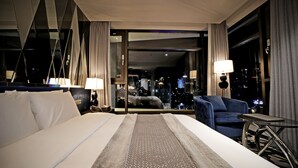 A hotel room with a large bed, a seating area with a blue sofa, and a view of the cityscape through the window.