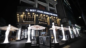 The exterior of the Best Louis Hamilton Hotel with illuminated signage, outdoor seating with umbrellas, and a modern architectural design.