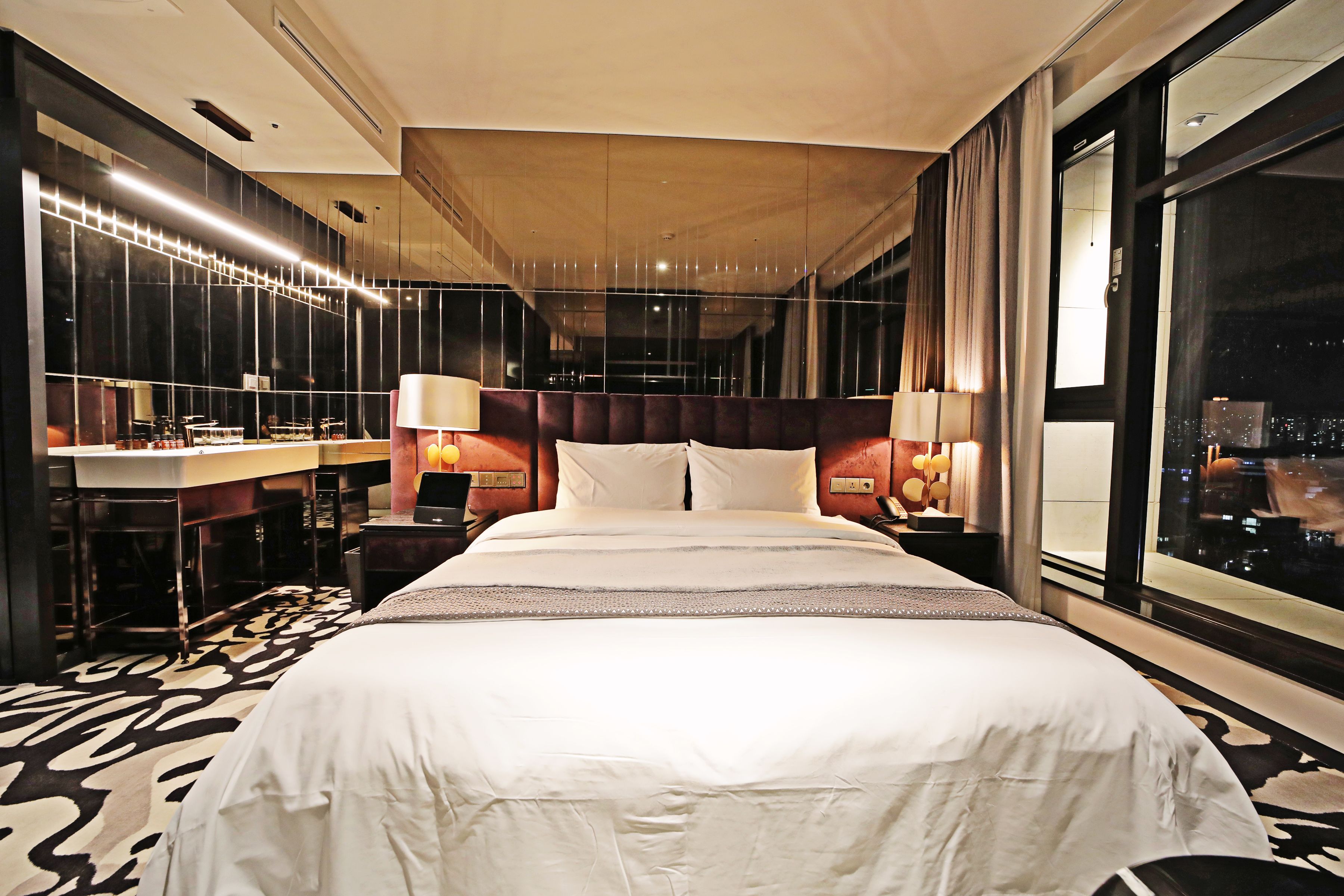 A hotel room with a large bed, a desk, and a view of the city at night.