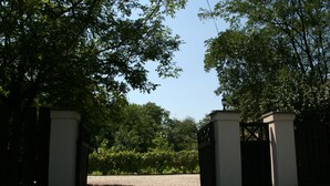 A gated entrance with a gravel path leading through a landscaped area with trees and shrubs. - Country house, 8 people. Private parking, swimming pool and large private garden. At Lake Tisza. (Tiszaszentimre)